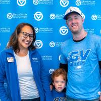 Man and woman with small child standing between them posing for picture in front of GV backdrop
